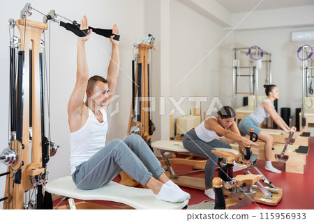 Sportive young guy training her arms pulling handle of cable exercise machine Sportive young guy training her arms pulling handle of cable exercise machine 115956933