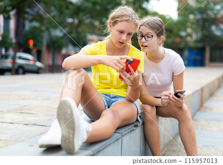 Teenager girls using smartphones while sitting in park 115957013