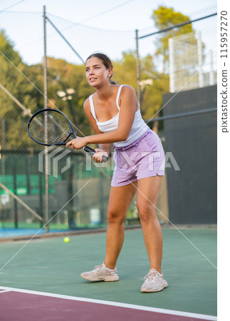 Focused young woman playing tennis on court, preparing to hit to return ball. Concept of sport training Focused young woman playing tennis on court, preparing to hit to return ball. Concept of sport training 115957270