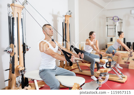 Sportive young guy training her arms pulling handle of cable exercise machine 115957315