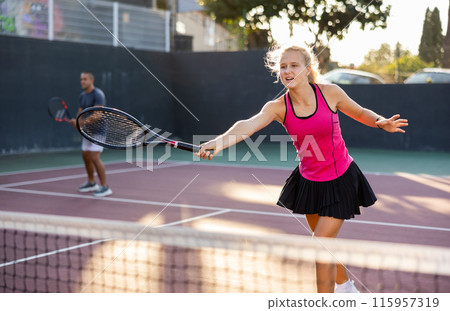 Sports active woman and her male partner playing tennis on court together during friendly match Sports active woman and her male partner playing tennis on court together during friendly match 115957319