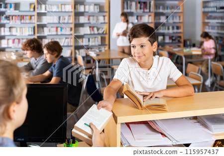 Ten-year-old schoolboy passes books to the librarian Ten-year-old schoolboy passes books to the librarian 115957437