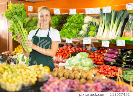 Teenage girl in uniform in grocery selling celery Teenage girl in uniform in grocery selling celery 115957491