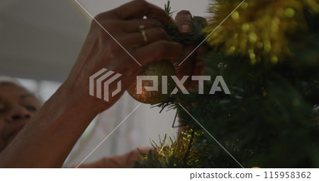 Senior biracial woman hanging ornaments on Christmas tree 115958362