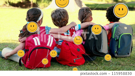 School friends sitting close, embracing, with backpacks on grass 115958830
