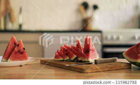 Triangular pieces of watermelon on a wooden cutting board on a kitchen background Triangular pieces of watermelon on a wooden cutting board on a kitchen background 115962788