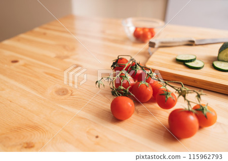 Slicing cherry tomatoes and cucumbers on a wooden cutting board 115962793