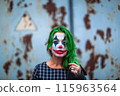 Portrait of a greenhaired girl in chekered dress with joker makeup on a rusty metal wall background. 115963564