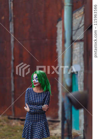 Portrait of a greenhaired girl in chekered dress with joker makeup on a rusty metal wall background. 115963566