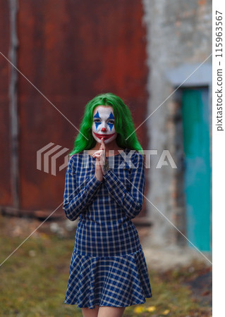 Portrait of a greenhaired girl in chekered dress with joker makeup on a rusty metal wall background. 115963567