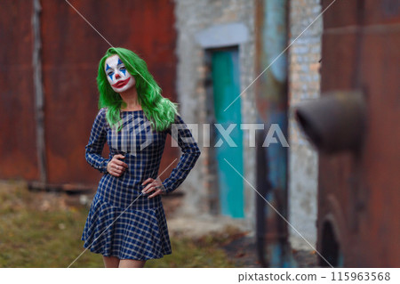 Portrait of a greenhaired girl in chekered dress with joker makeup on a rusty metal wall background. 115963568