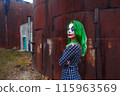 Portrait of a greenhaired girl in chekered dress with joker makeup on a rusty metal wall background. 115963569