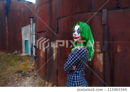 Portrait of a greenhaired girl in chekered dress with joker makeup on a rusty metal wall background. 115963569