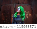 Portrait of a greenhaired girl in chekered dress with joker makeup on a rusty metal wall background. 115963571