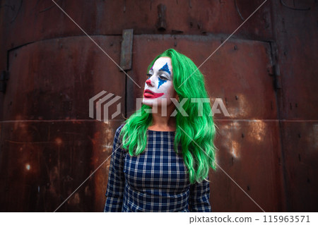 Portrait of a greenhaired girl in chekered dress with joker makeup on a rusty metal wall background. Portrait of a greenhaired girl in chekered dress with joker makeup on a rusty metal wall background. 115963571