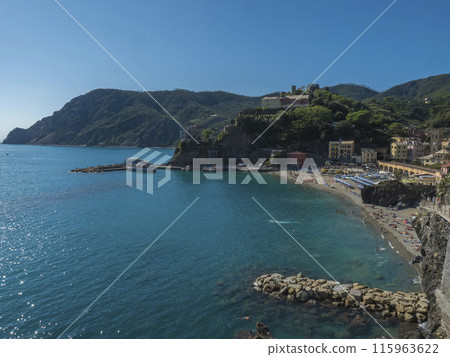 Picturesque view of Monterosso al Mare with beach, colorful houses, train rails, bell tower and Torre Bastioni with green cliffs, clear blue sky and sea. National park Cinque Terre, Liguria, Italy 115963622