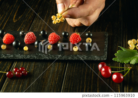 A man's hand adds ribes to a black sorting board before serving for dessert. Low-key berry diet concept A man's hand adds ribes to a black sorting board before serving for dessert. Low-key berry diet concept 115963910
