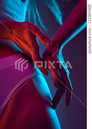 Close-up of woman's hands on her hips in white underwear in pink neon light against gradient background. Spa treatment Close-up of woman's hands on her hips in white underwear in pink neon light against gradient background. Spa treatment 115965006