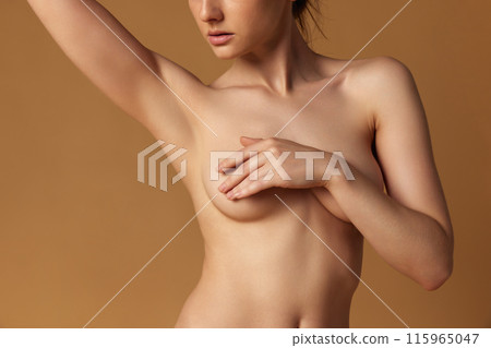 Close up photo of young woman covered her breast against sandy studio background. Prevention of cancer Close up photo of young woman covered her breast against sandy studio background. Prevention of cancer 115965047