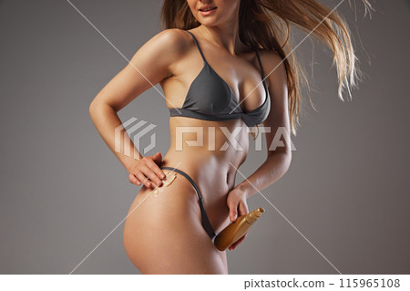 Photo of woman in swimsuit applying lotion to protect skin from sun beams against warm grey studio background. Cosmetic products. Photo of woman in swimsuit applying lotion to protect skin from sun beams against warm grey studio background. Cosmetic products. 115965108