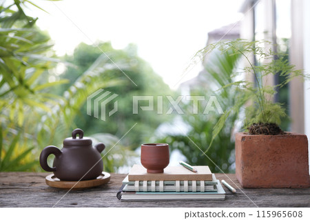 Tea cup and earthenware teapot and notebooks at the balcony and plant pot at balcony outdoor Tea cup and earthenware teapot and notebooks at the balcony and plant pot at balcony outdoor 115965608