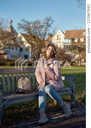 Winter Joy in Bitigheim-Bissingen: Beautiful Girl in Pink Jacket Sitting Amidst Half-Timbered Charm. beautiful girl in a pink winter jacket sitting on a bench in a park, set against the backdrop of Winter Joy in Bitigheim-Bissingen: Beautiful Girl in Pink Jacket Sitting Amidst Half-Timbered Charm. beautiful girl in a pink winter jacket sitting on a bench in a park, set against the backdrop of 115967681