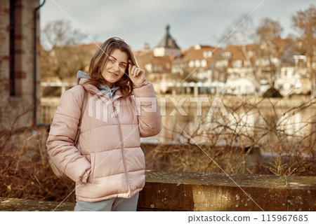 Young beautiful pretty tourist girl in warm hat and coat with backpack walking at cold autumn in Europe city enjoying her travel in Bietigheim-Bissingen, Deutschland. Outdoor portrait of young tourist 115967685