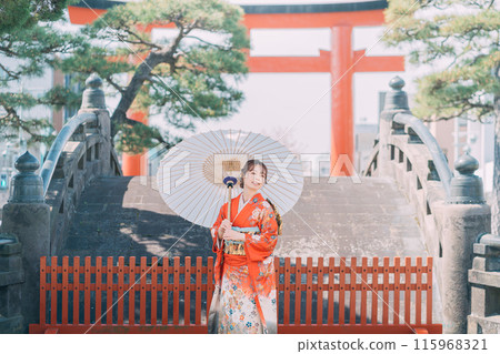 A woman in a long-sleeved kimono standing at the torii gate of a shrine A woman in a long-sleeved kimono standing at the torii gate of a shrine 115968321