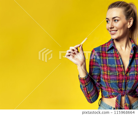 Smiling Young Woman Holding French Fry on Yellow Background 115968664