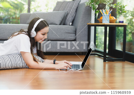 Pretty young woman wear headphones lying down on floor and usinging laptop. Distance learning. Remote work place. Quarantine, coronovirus pandemic covid-19. Pretty young woman wear headphones lying down on floor and usinging laptop. Distance learning. Remote work place. Quarantine, coronovirus pandemic covid-19. 115968939
