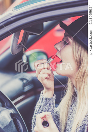 Young woman applying lipstick in car 115969634