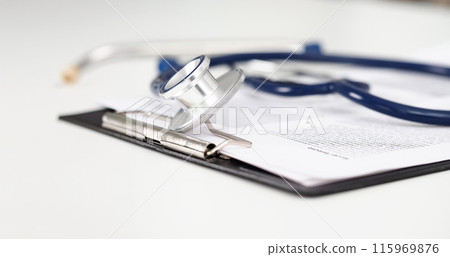 Stethoscope head lying on medical form on clipboard pad 115969876