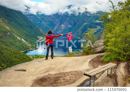 Tourist over Geirangerfjord holds norwegian flag Tourist over Geirangerfjord holds norwegian flag 115970091