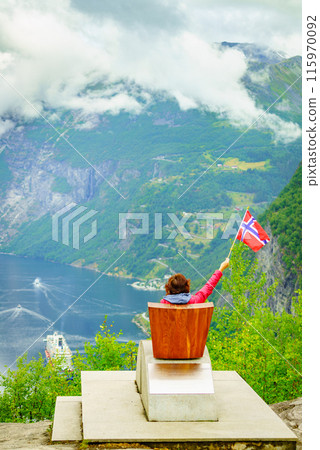 Tourist over Geirangerfjord holds norwegian flag Tourist over Geirangerfjord holds norwegian flag 115970092