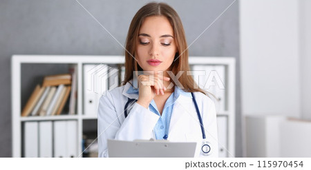 Beautiful smiling female doctor stand in office Beautiful smiling female doctor stand in office 115970454