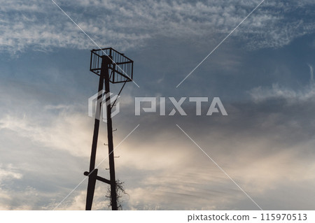 A calm and serene scene with the silhouette of a simple tower structure against a softly lit sky. The tower with a vertical pole and horizontal crossbars leads to a small platform. A calm and serene scene with the silhouette of a simple tower structure against a softly lit sky. The tower with a vertical pole and horizontal crossbars leads to a small platform. 115970513
