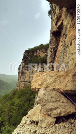 Stratified Cliffside Landscape. A rugged cliffside showcasing stratified sedimentary rock formations, surrounded by forested area under an overcast sky. Stratified Cliffside Landscape. A rugged cliffside showcasing stratified sedimentary rock formations, surrounded by forested area under an overcast sky. 115970570