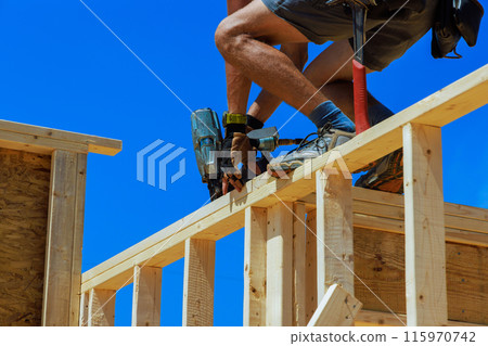 Working with an air nail hammer, framing contractor nails wooden beams Working with an air nail hammer, framing contractor nails wooden beams 115970742