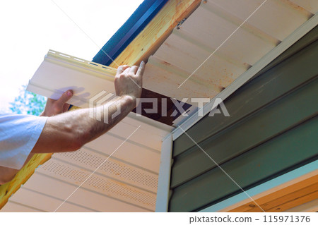 Installing vinyl soffit plastic panels on facade ceiling of new house by an employee Installing vinyl soffit plastic panels on facade ceiling of new house by an employee 115971376