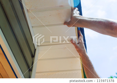 Installing vinyl soffit plastic panels on facade ceiling of new home by an employee 115971378