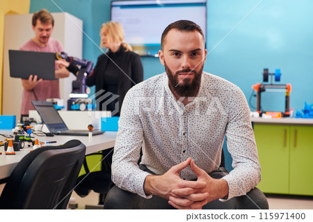 A man sitting in a robotics laboratory while his colleagues in the background test new, cutting edge robotic inventions. A man sitting in a robotics laboratory while his colleagues in the background test new, cutting edge robotic inventions. 115971400