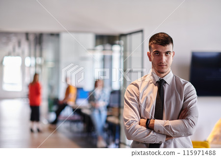 A young business leader stands with crossed arms in a modern office hallway, radiating confidence and a sense of purpose, embodying a dynamic and inspirational presence. A young business leader stands with crossed arms in a modern office hallway, radiating confidence and a sense of purpose, embodying a dynamic and inspirational presence. 115971488