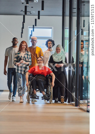 A diverse group of young business people walking a corridor in the glass-enclosed office of a modern startup, including a person in a wheelchair and a woman wearing a hijab, showing a dynamic mix of 115971515