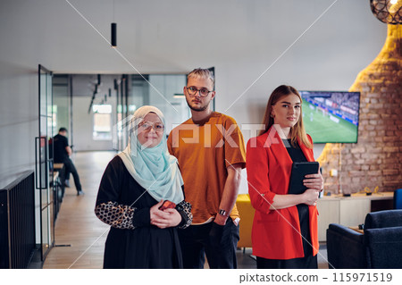 A group of young business colleagues, including a woman in a hijab, stands united in the modern corridor of a spacious startup coworking center, representing diversity and collaborative spirit. 115971519