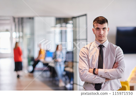 A young business leader stands with crossed arms in a modern office hallway, radiating confidence and a sense of purpose, embodying a dynamic and inspirational presence. A young business leader stands with crossed arms in a modern office hallway, radiating confidence and a sense of purpose, embodying a dynamic and inspirational presence. 115971550