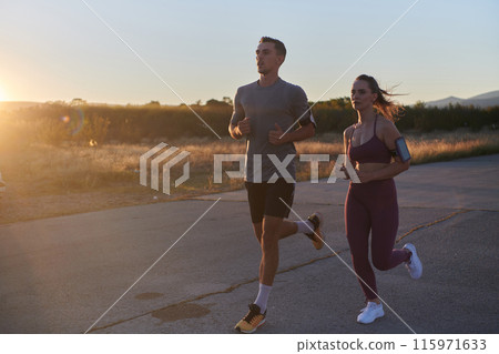 A handsome young couple running together during the early morning hours, with the mesmerizing sunrise casting a warm glow, symbolizing their shared love and vitality 115971633