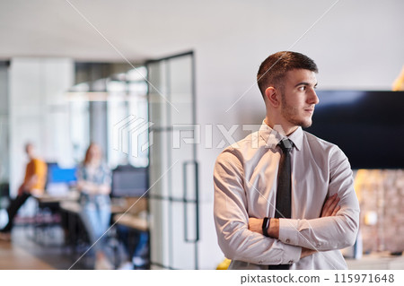 A young business leader stands with crossed arms in a modern office hallway, radiating confidence and a sense of purpose, embodying a dynamic and inspirational presence. A young business leader stands with crossed arms in a modern office hallway, radiating confidence and a sense of purpose, embodying a dynamic and inspirational presence. 115971648