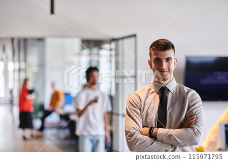 A young business leader stands with crossed arms in a modern office hallway, radiating confidence and a sense of purpose, embodying a dynamic and inspirational presence. A young business leader stands with crossed arms in a modern office hallway, radiating confidence and a sense of purpose, embodying a dynamic and inspirational presence. 115971795