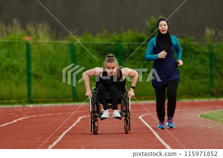 A Muslim woman in a burqa running together with a woman in a wheelchair on the marathon course, preparing for future competitions. 115971852