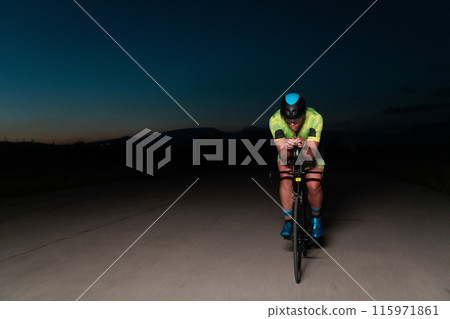 A triathlete rides his bike in the darkness of night, pushing himself to prepare for a marathon. The contrast between the darkness and the light of his bike creates a sense of drama and highlights the A triathlete rides his bike in the darkness of night, pushing himself to prepare for a marathon. The contrast between the darkness and the light of his bike creates a sense of drama and highlights the 115971861